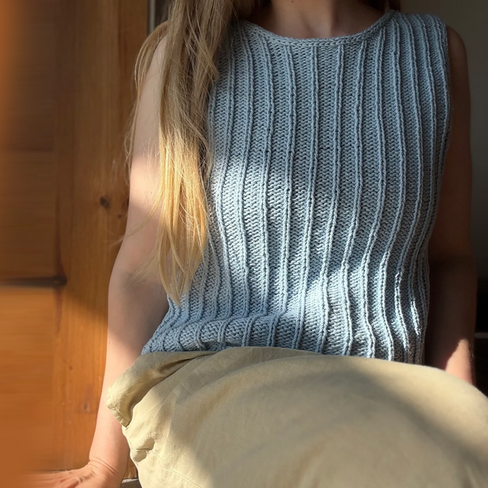 Person wearing a blue knitted sleeveless top -Granular top by aegyoknit  - sitting on a wooden bench 